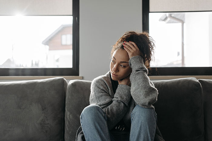 A distressed woman with curly hair sits on a sofa, portraying true crime fans sensing something seriously wrong.