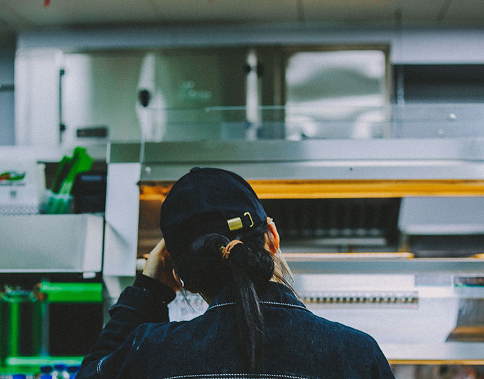A woman with her back to the camera, wearing a cap, looks at shelves, a scene relatable to true crime fans.