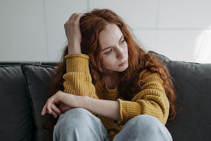 A redhead woman with long hair sitting on a couch, looking pensive, representing a true crime fan realizing something is wrong.
