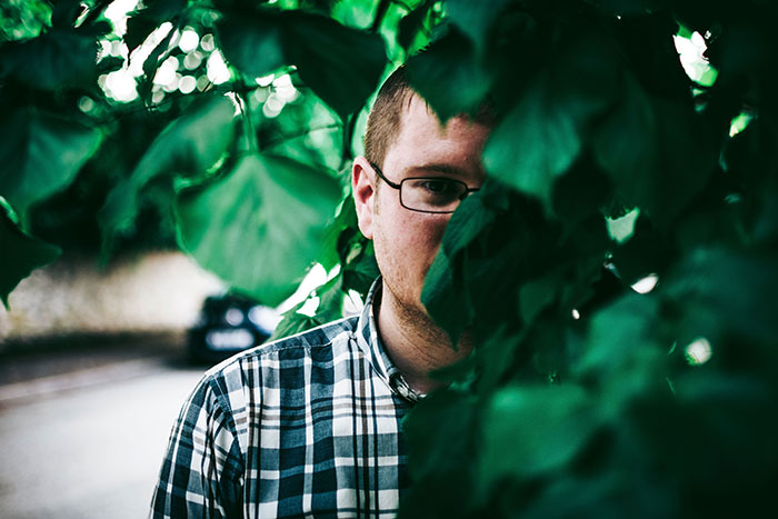 A man peeking from behind green leaves, showing only half his face, illustrating a moment of true crime realization.