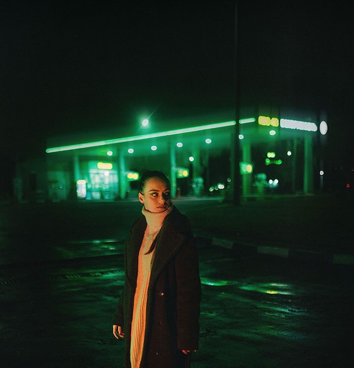 A woman in a dark coat stands at a gas station at night, realizing something was seriously wrong.