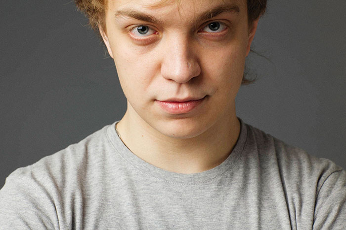 A young man with light brown hair and blue eyes looks intently, like true crime fans.