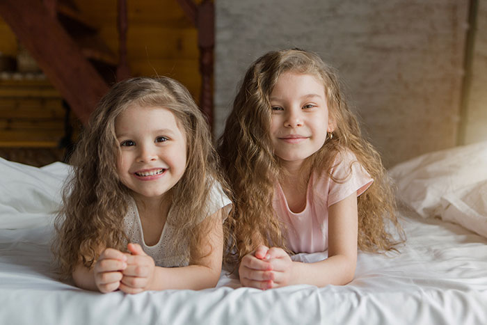 Two smiling young girls with curly hair lying on a bed indoors Two smiling young girls with curly hair lying on a bed indoors