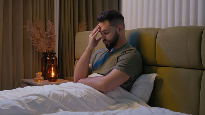 Man in bed with a hand on his head, looking stressed about fainting at a concert. Man in bed with a hand on his head, looking stressed about fainting at a concert.