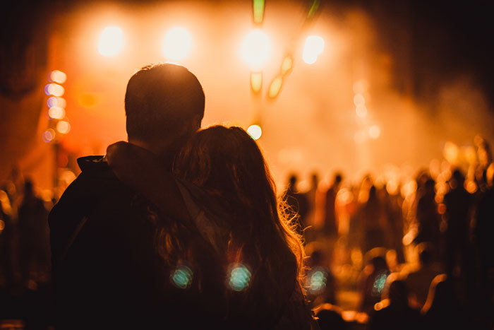 A couple embracing at a concert, with bright lights and a crowd visible, before man wants to go home. A couple embracing at a concert, with bright lights and a crowd visible, before man wants to go home.