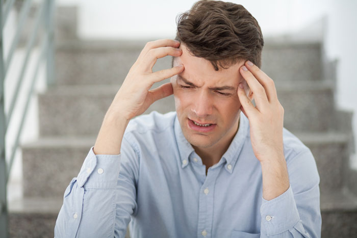 A man holds his head in pain, representing the man fainting at a concert. A man holds his head in pain, representing the man fainting at a concert.