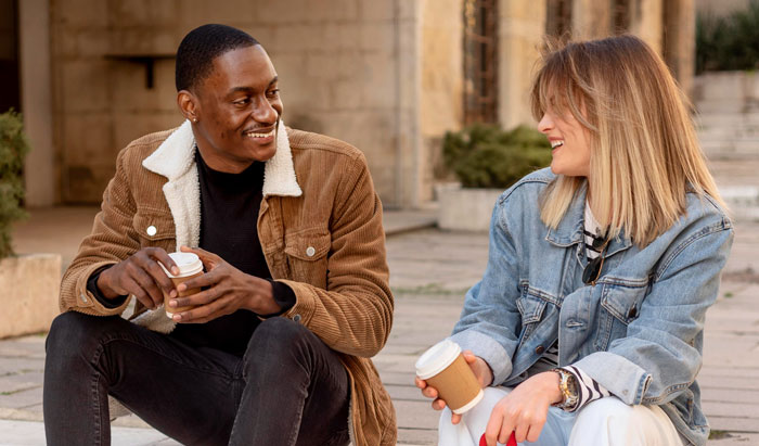 Man and woman smiling while holding coffee and sitting outside Man and woman smiling while holding coffee and sitting outside
