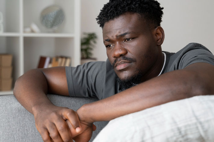 Pensive man sitting on couch deep in thought at home Pensive man sitting on couch deep in thought at home