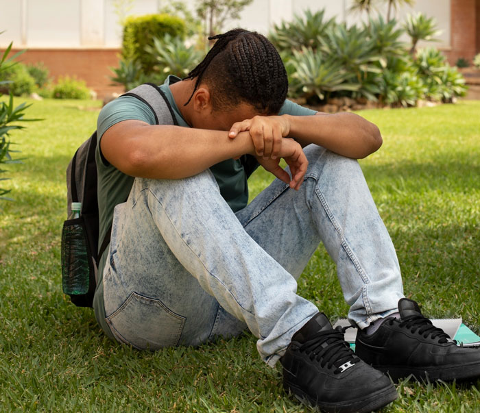 Teen boy sitting on grass looking upset, recalling school bully experiences Teen boy sitting on grass looking upset, recalling school bully experiences