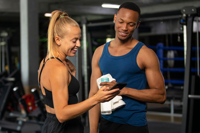 Man and woman smiling and looking at phone together in gym setting Man and woman smiling and looking at phone together in gym setting