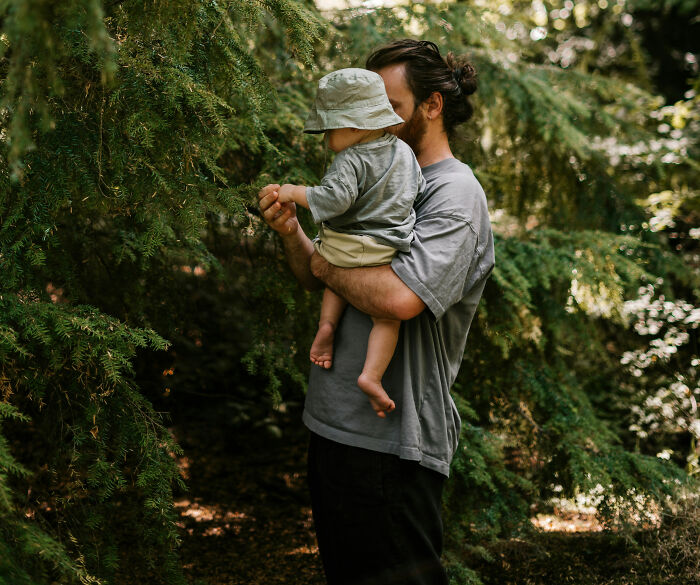 Father holding baby exploring nature with trees in background