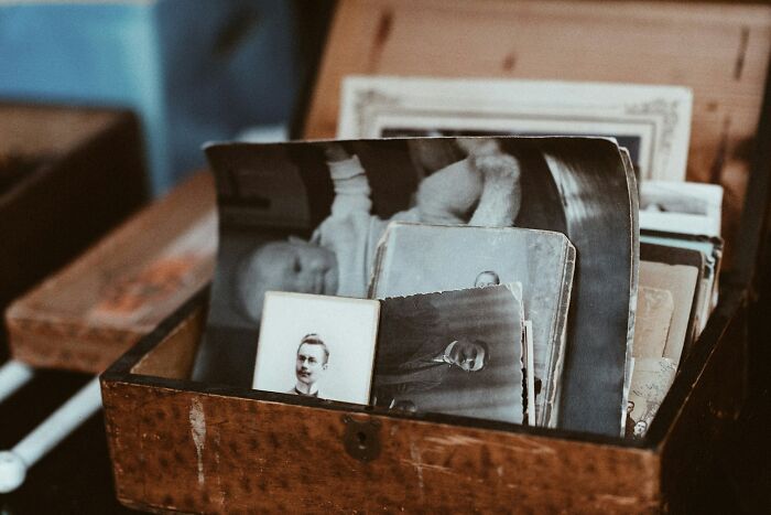 An old wooden box filled with vintage photographs, symbolizing exposed double lives and hidden pasts.