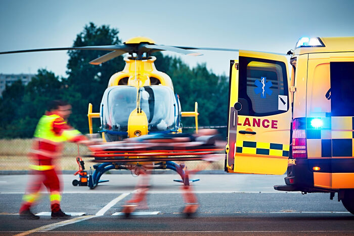 Emergency personnel with a stretcher by a helicopter and ambulance, after a car accident.