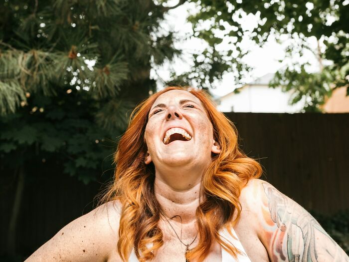 Woman laughing joyfully in sunlight surrounded by trees for emotional healing
