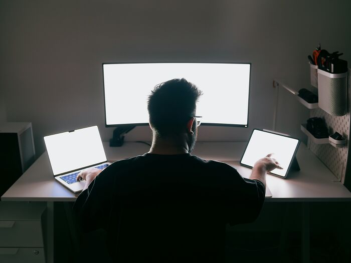 Man working with multiple glowing screens at desk in dark room petty revenge stories