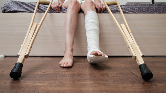 A disabled teen with a broken leg in a cast, sitting on a bed with crutches, facing challenges with school access.