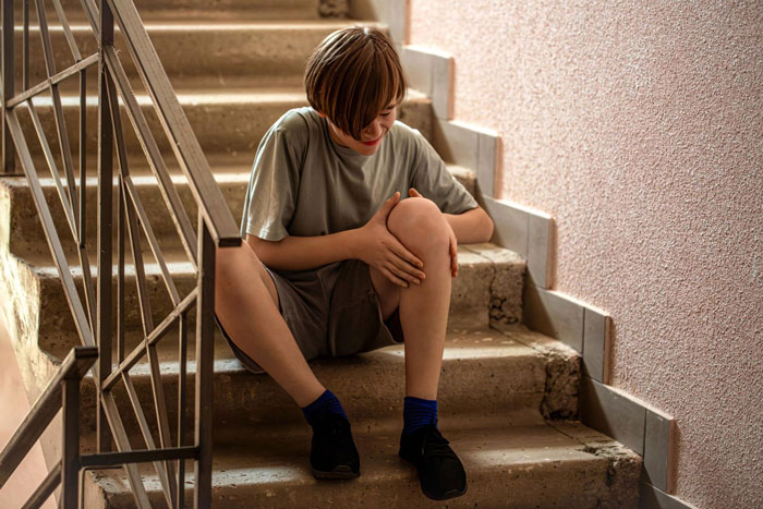 A disabled teen sits on school stairs, clutching his knee in pain, highlighting the need for an elevator key.
