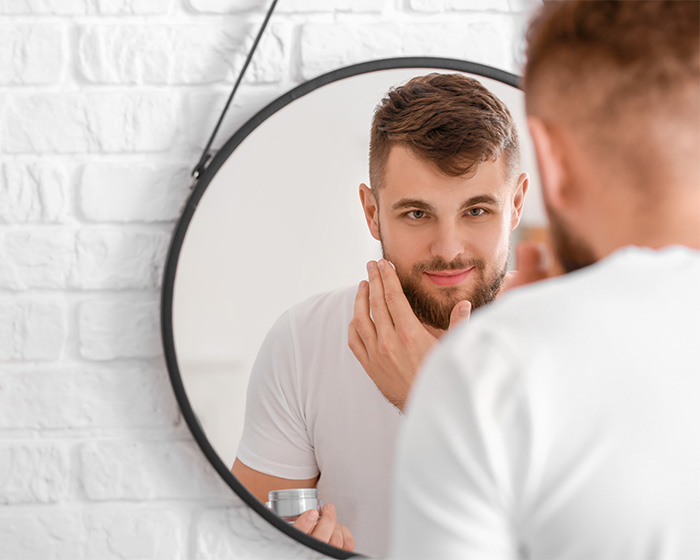 Man looking in mirror with skincare cream, demonstrating male attractiveness care Man looking in mirror with skincare cream, demonstrating male attractiveness care