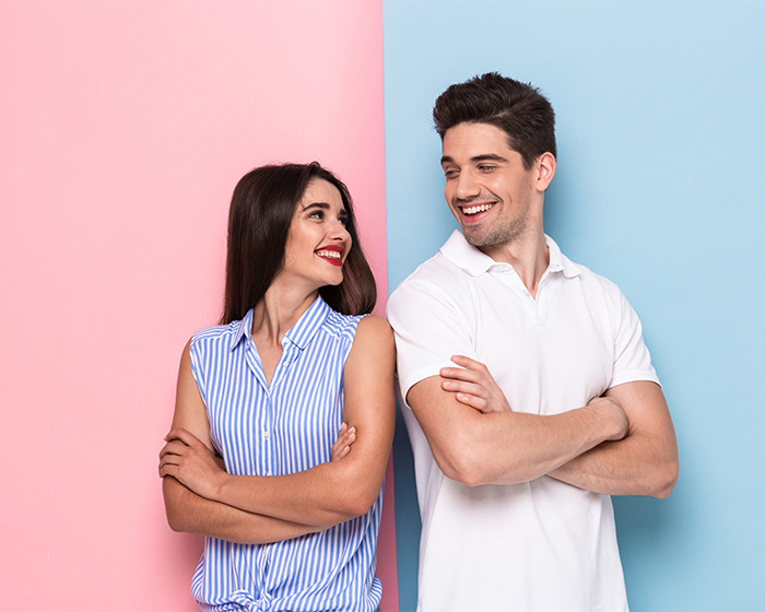 Smiling young woman and man standing back to back against pink and blue backgrounds Smiling young woman and man standing back to back against pink and blue backgrounds