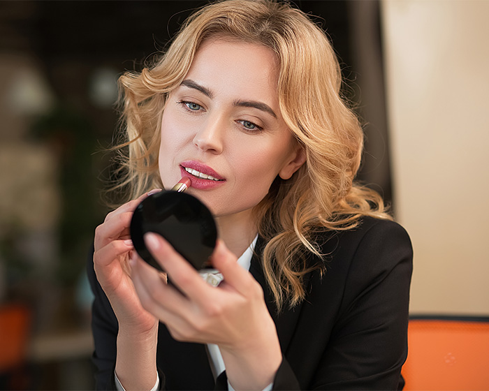 Blonde woman applying lipstick symbolizing female attractiveness Blonde woman applying lipstick symbolizing female attractiveness