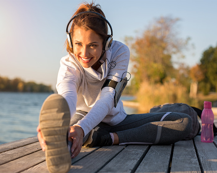 Woman exercising outdoors stretching leg with headphones by water Woman exercising outdoors stretching leg with headphones by water