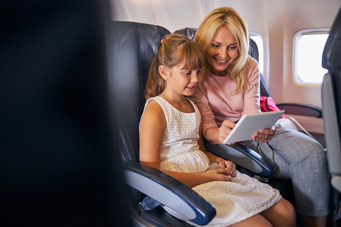 Woman and girl smiling using tablet while seated on airplane Woman and girl smiling using tablet while seated on airplane