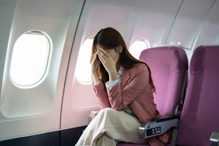 Woman stressed on airplane seat covering face, airplane seat disruption scenario Woman stressed on airplane seat covering face, airplane seat disruption scenario