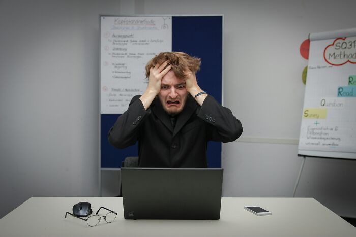 Stressed man holding his head in frustration working on laptop, showing anxiety thought patterns in psychology