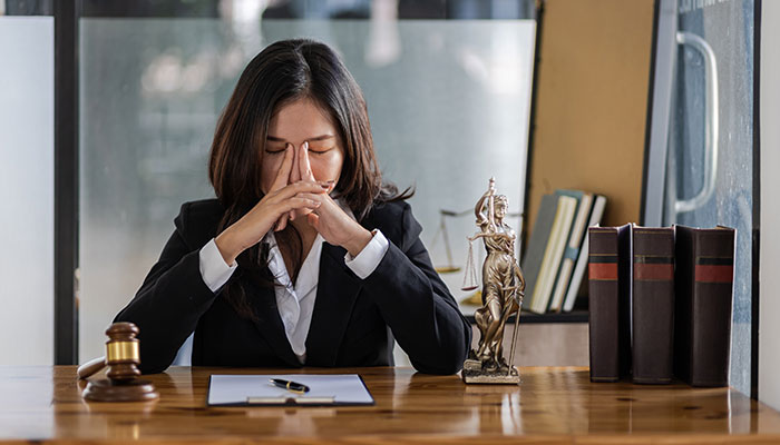 A stressed woman at a desk with legal items, symbolizing the burden of secrets people keep to themselves.