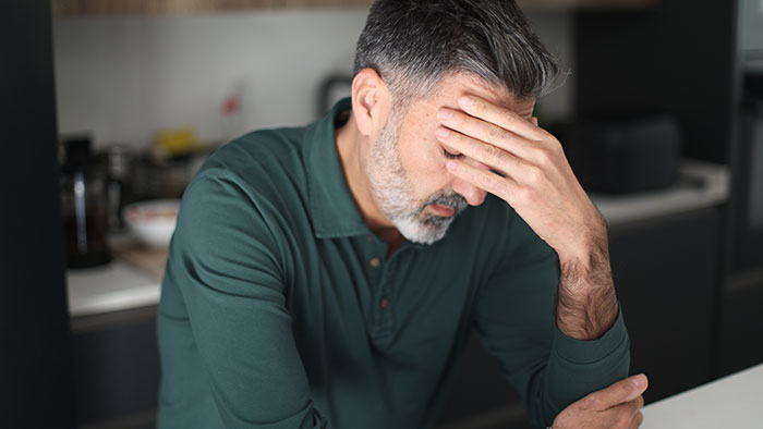 A man with his hand on his forehead, looking stressed, possibly burdened by secrets people keep to themselves.