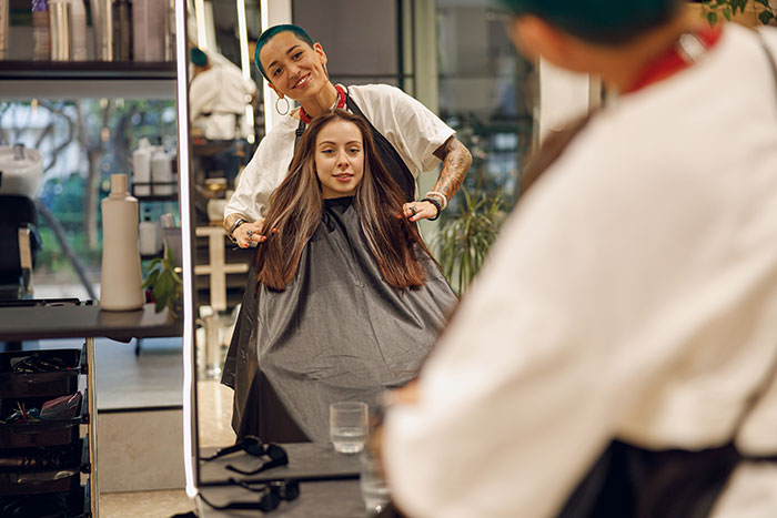 Hair stylist cutting a client's hair in a salon, keeping secrets about others to themselves.