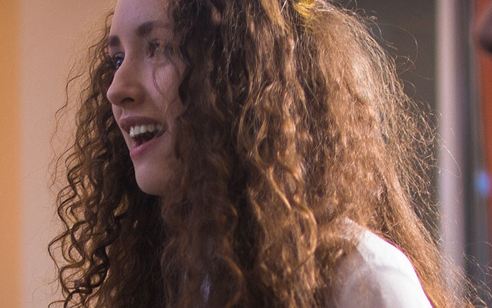 A happy woman with curly hair, keeping secrets about others to themselves.