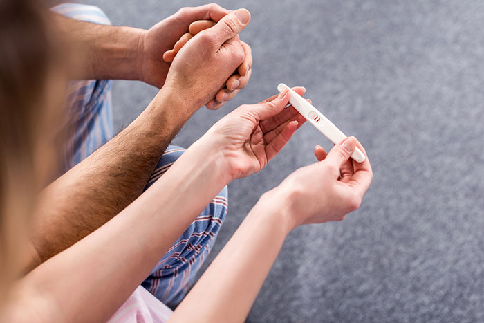 A couple holding hands, looking at a pregnancy test, a moment that might involve secrets people keep to themselves.