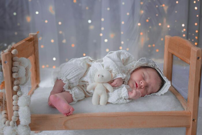 A newborn baby in white clothes sleeps peacefully in a small wooden bed, a depiction of strange jobs.