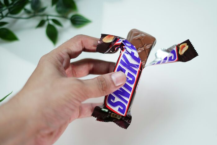 Hand holds unwrapped Snickers chocolate bar showing peanut caramel inside