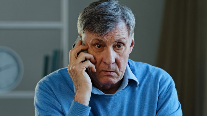 An older man on the phone, looking concerned, representing the family drama of a woman buying her own home.
