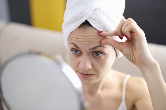 Woman with towel on head examining forehead wrinkles in mirror filler botox Woman with towel on head examining forehead wrinkles in mirror filler botox