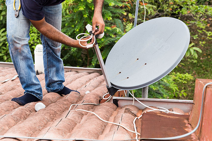 Man installing satellite dish on rooftop with cables