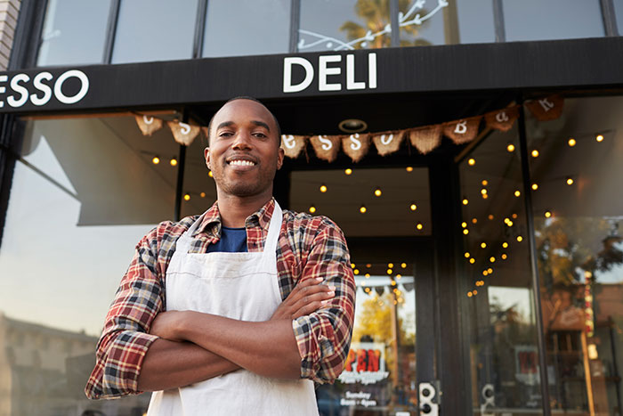 Smiling deli worker in apron standing outside shop entrance