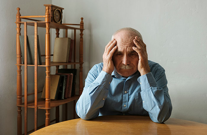 Worried elderly man sitting at table with hands on head