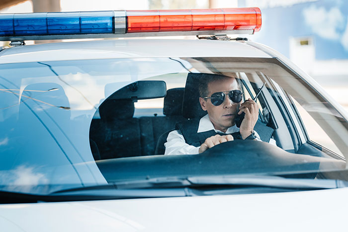 Police officer in car using radio fitting smooth criminals theme