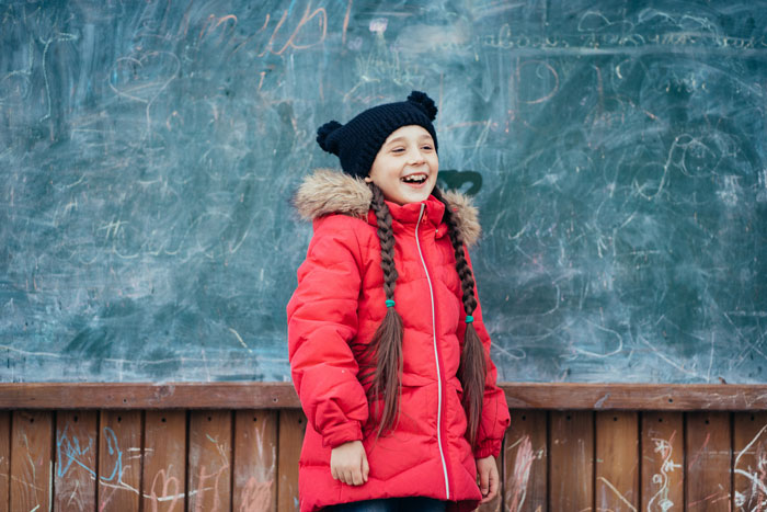 Smiling girl in red winter coat standing in front of chalkboard Smiling girl in red winter coat standing in front of chalkboard
