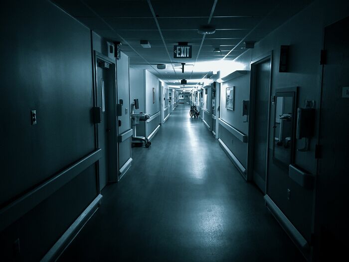 Dark empty hospital hallway with wheelchair and exit sign