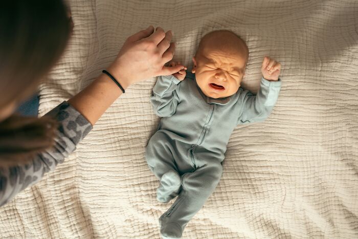 Crying newborn baby lying on blanket with adult hand nearby