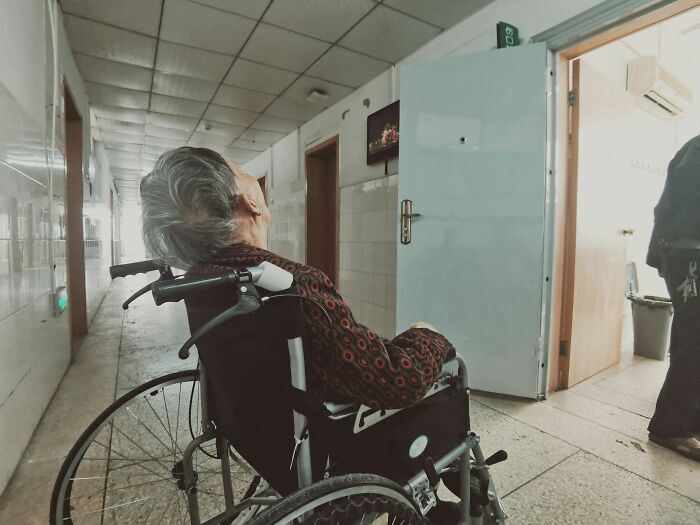 Elderly person in wheelchair looking up in hospital corridor