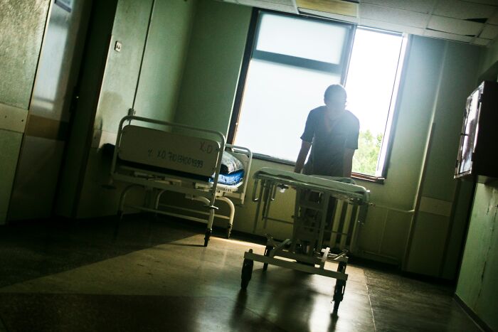 Creepy hospital room with empty bed and silhouette of person near window