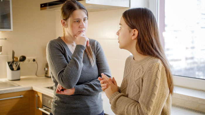 A mother and her 19-year-old stepdaughter talking in a kitchen, discussing house rules and difficult family contact. A mother and her 19-year-old stepdaughter talking in a kitchen, discussing house rules and difficult family contact.
