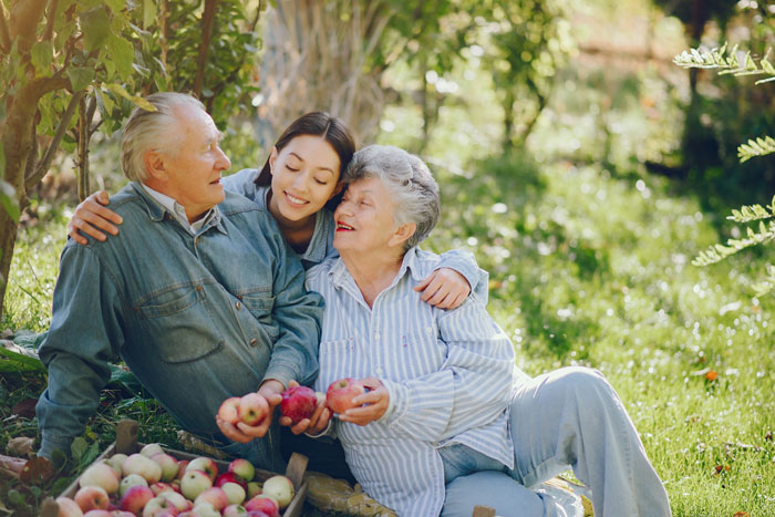 Teen smiling with grandparents harvesting apples outside