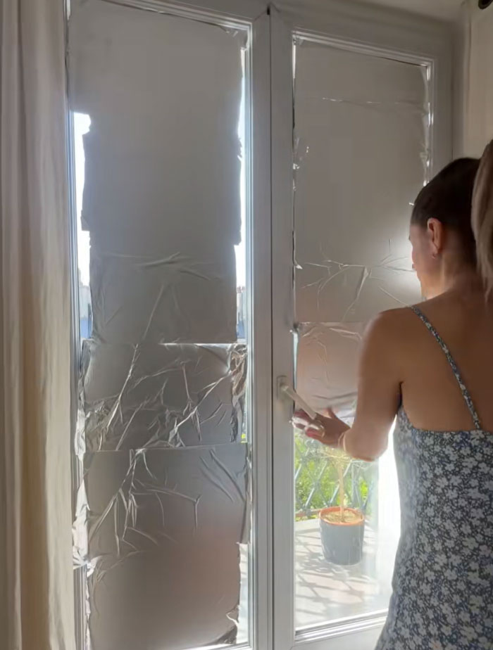 A person applying aluminum foil to windows to block out sun and survive the heatwave.