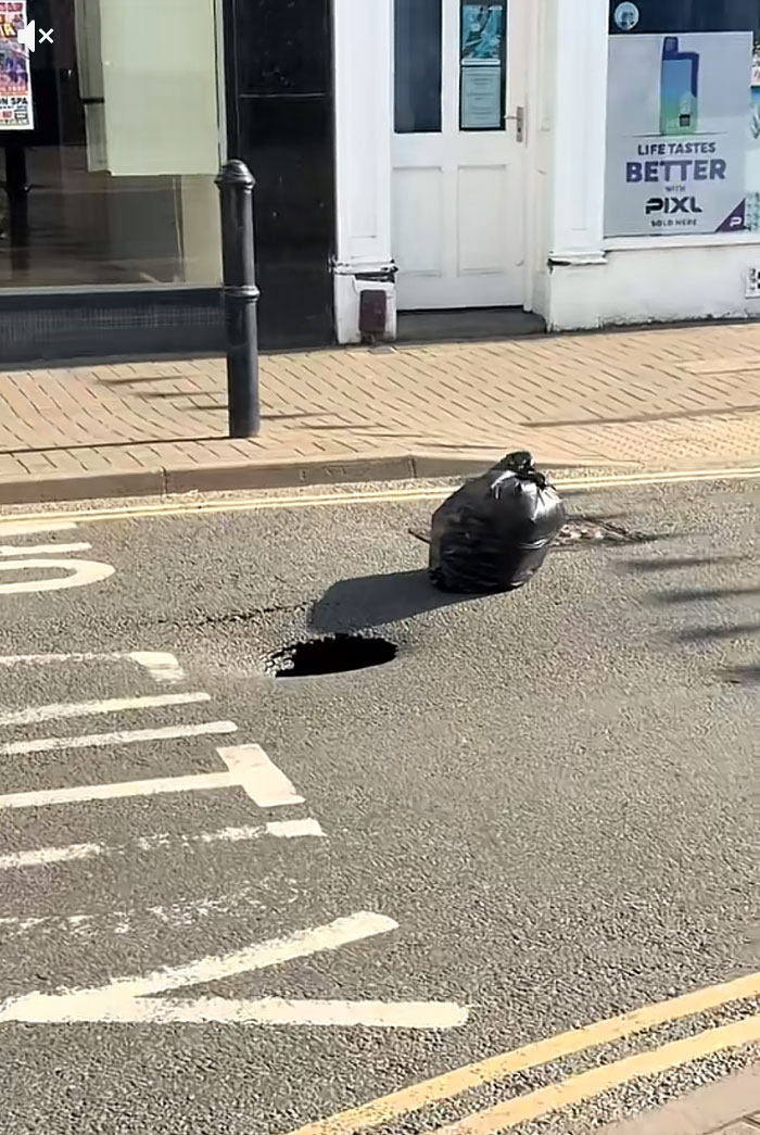 A black trash bag next to a sinkhole in a street, illustrating Europeans trying to survive the heatwave.